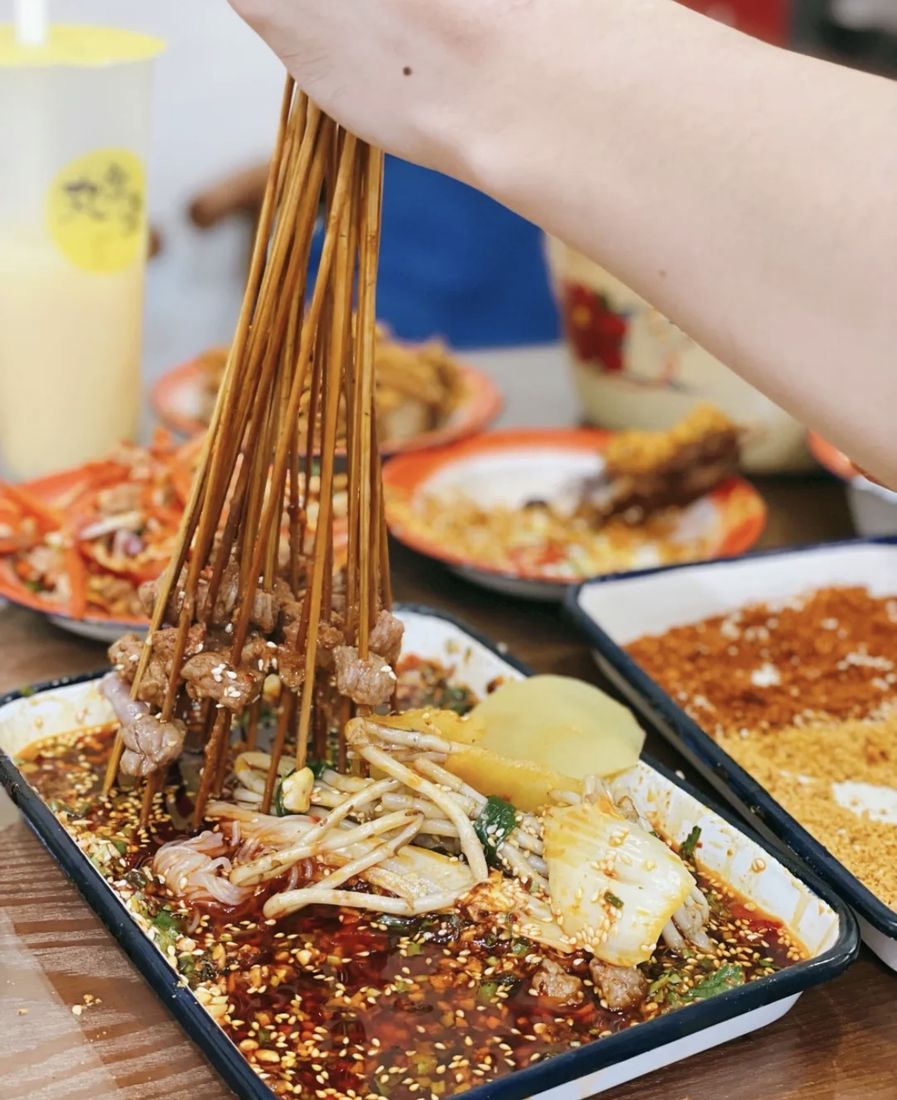 Skewers being lifted from a cold-pot dinner spread, a Chengdu street-food specialty