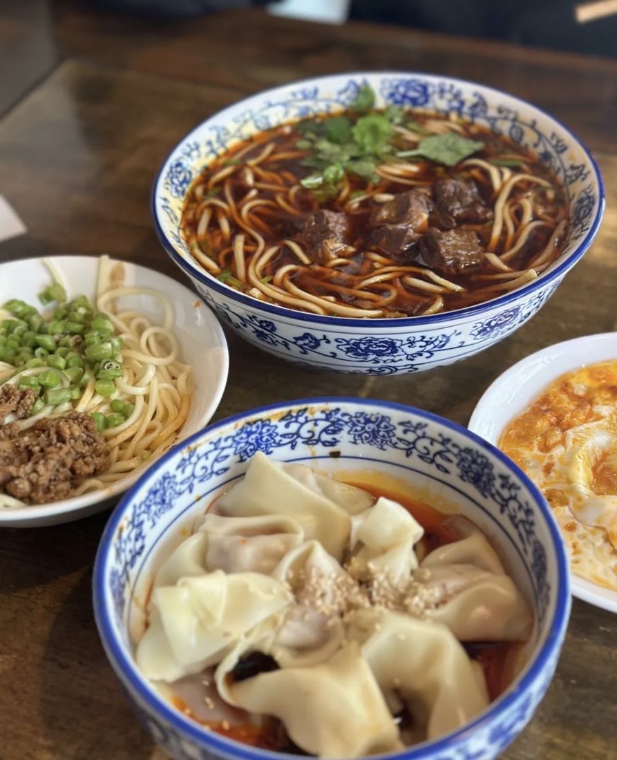 A spread of Chengdu noodle and dumpling bowls on a wooden table